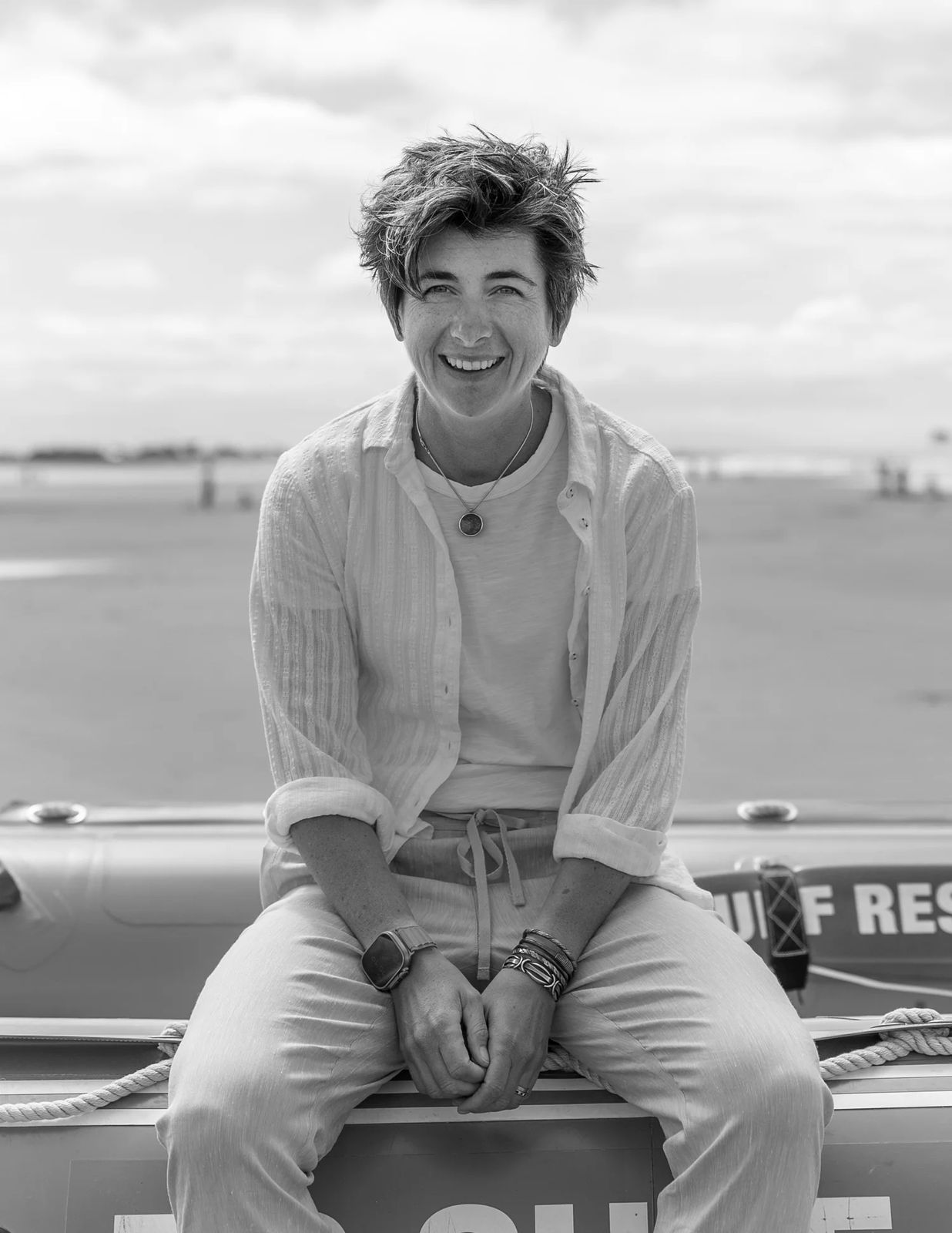 Poppie Johnson smiling, sitting on a life raft at the beach.
